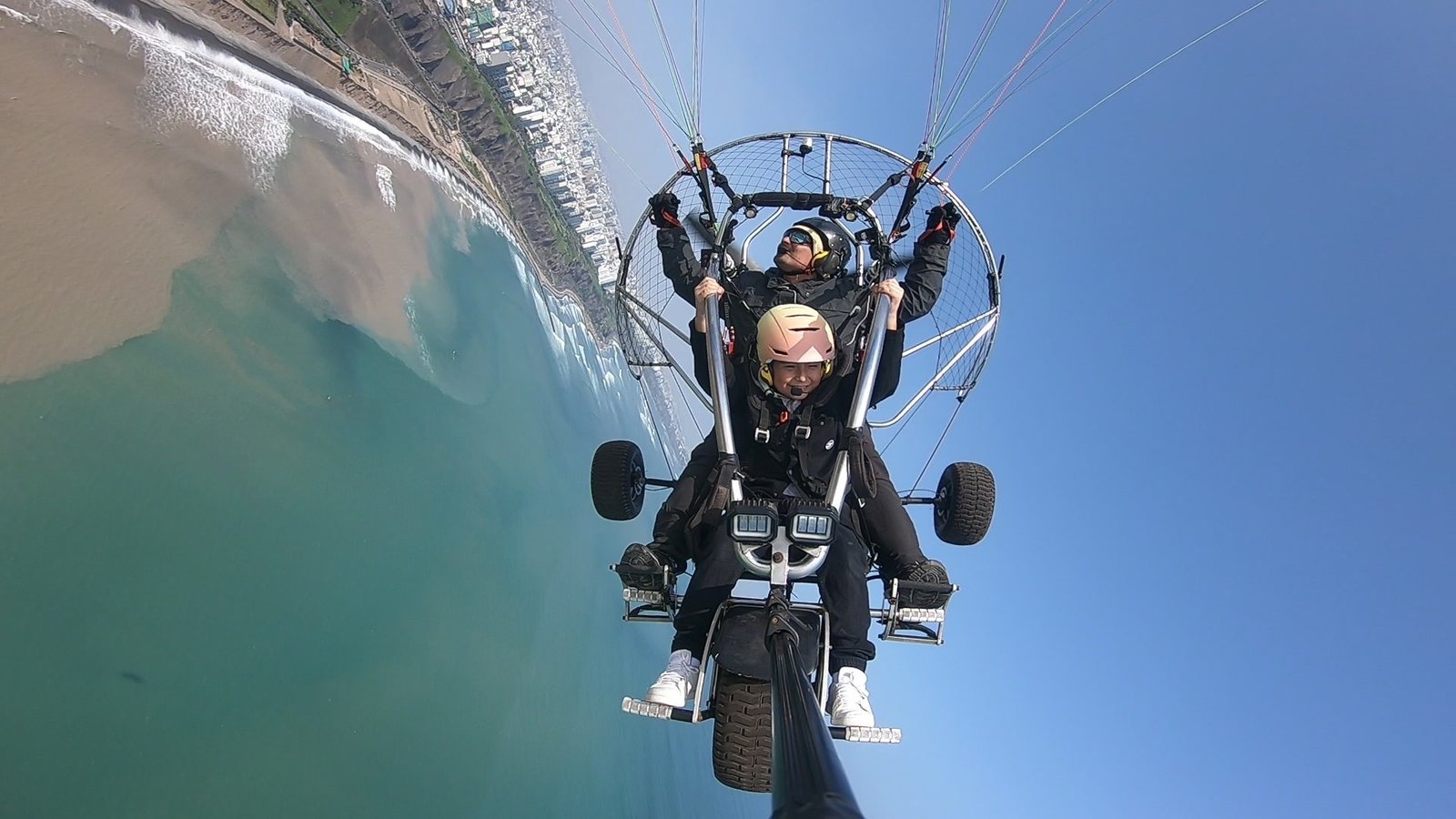 Pasajero sonriendo y levantando los brazos mientras vuela en paratrike sobre la Costa Verde de Lima con KunturFly
