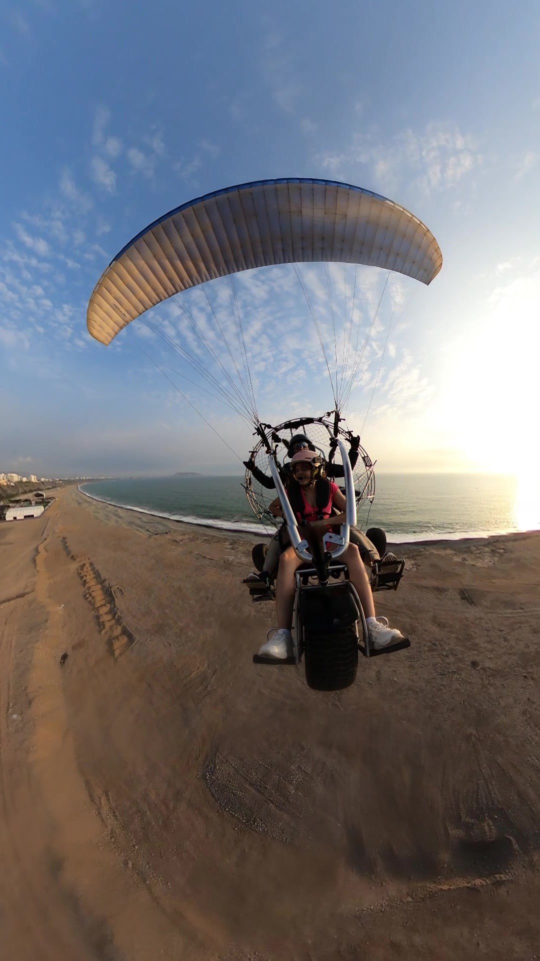 Paratrike biplaza al atardecer sobre playa de Lima, Perú, con horizonte marino y luz dorada, experiencia turística segura