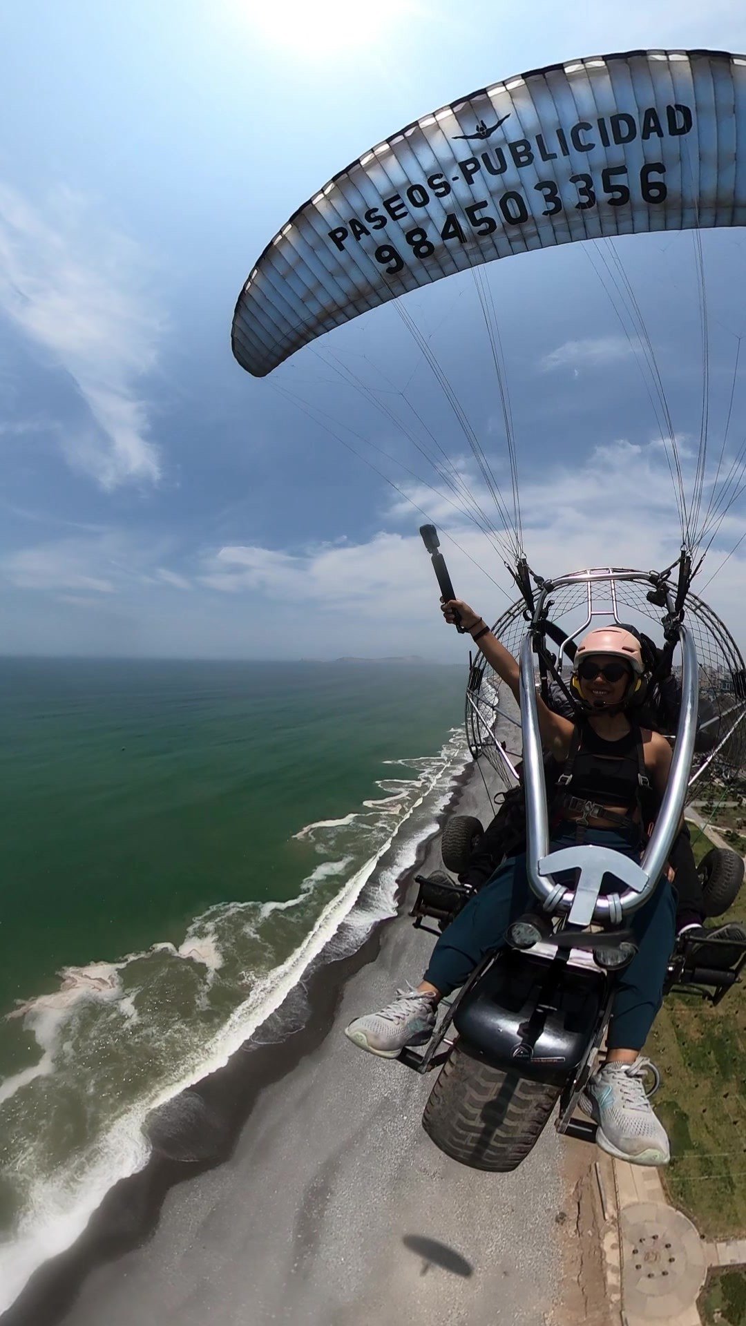 Pasajera fotografiando la costa limeña desde un vuelo en paratrike biplaza con vistas a acantilados y playas