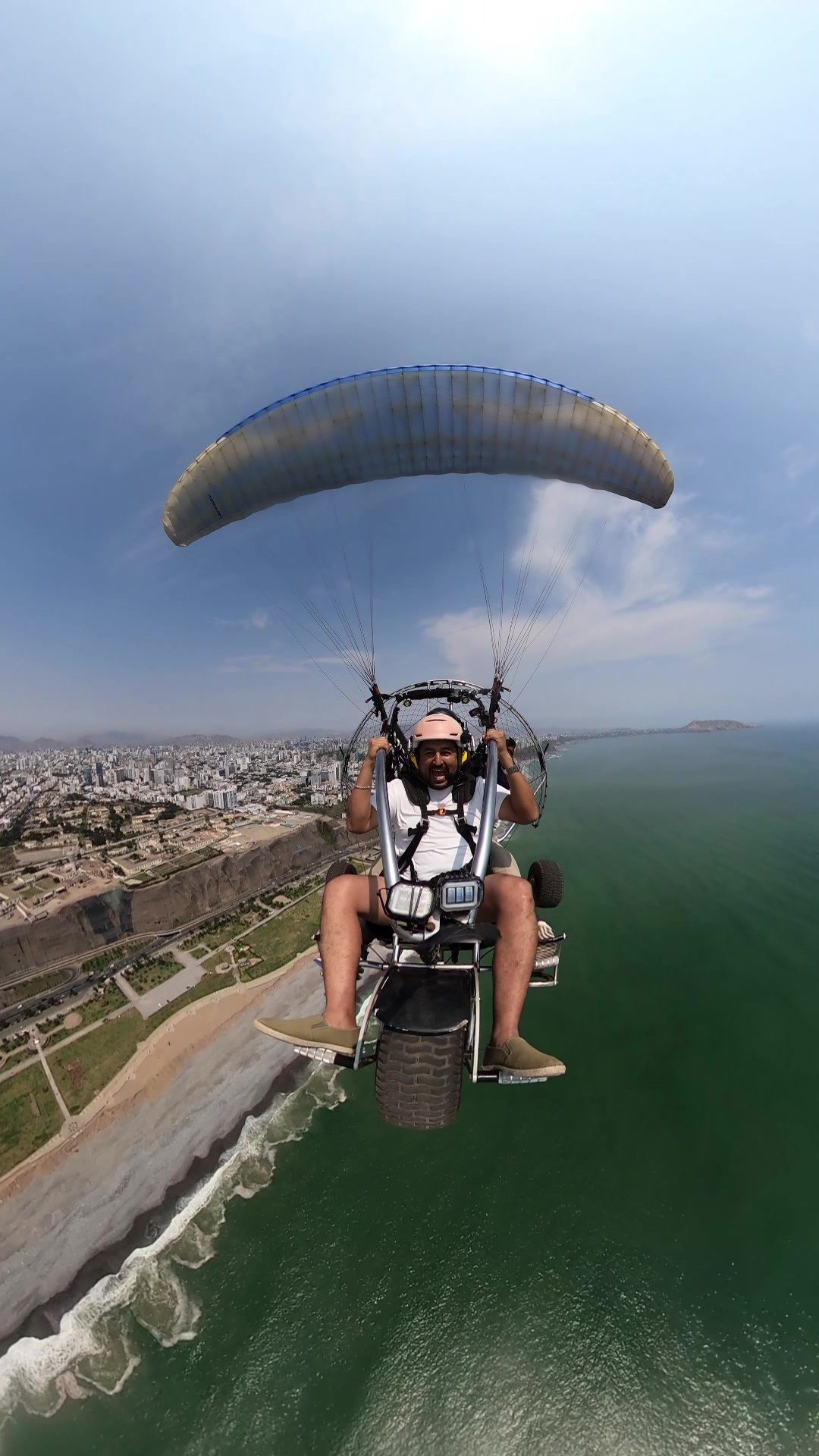 Vuelo en paratrike sobre el mar de Lima con pasajero sonriente y vista panorámica de la ciudad